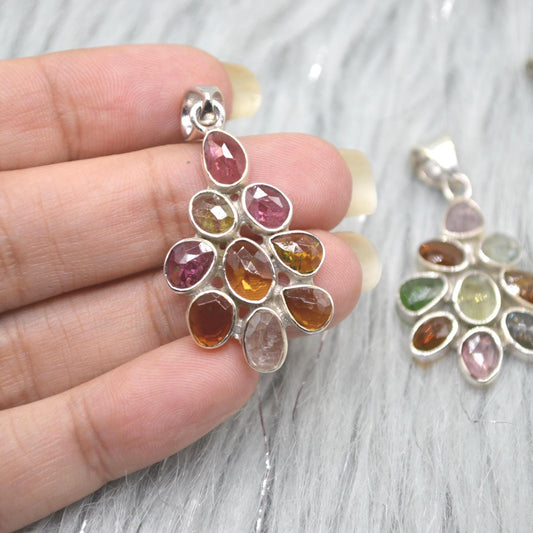 May include: A silver pendant featuring a cluster of colourful gemstones in shades of pink, orange, brown, and green. The gemstones are teardrop and oval-shaped, set in a silver metal setting. The pendant is designed to be worn as jewellery.